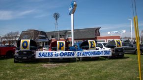 Car dealership lot with a sign that says "Open. Slaes is Open by appointment only."