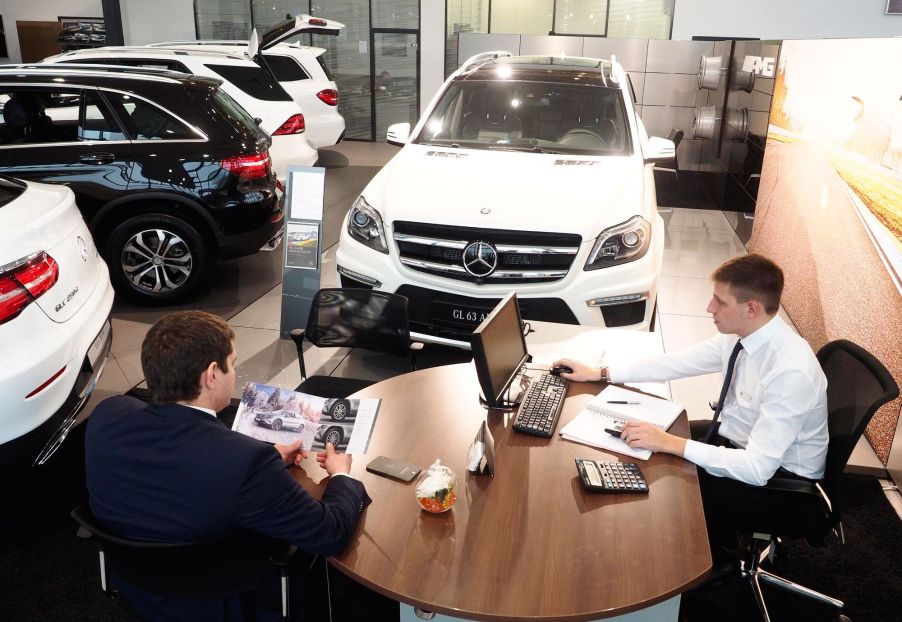 A car sales man sits with a customer at a dealership.