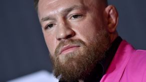 Conor McGregor in a a pink suit and black shirt in front of a grey background.