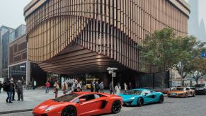 A red Ferrari and a light blue Lamborghini in front of a modern shaped tall building.