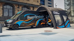 The Team Fordzilla Gaming Transit van in black with a blue and orange livery. At the rear of the van is an inflatable pop-up canopy with a similar blue and orange "wavy" livery that is featured on the van