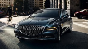 A dark colored 2021 Genesis G80 driving through a city.