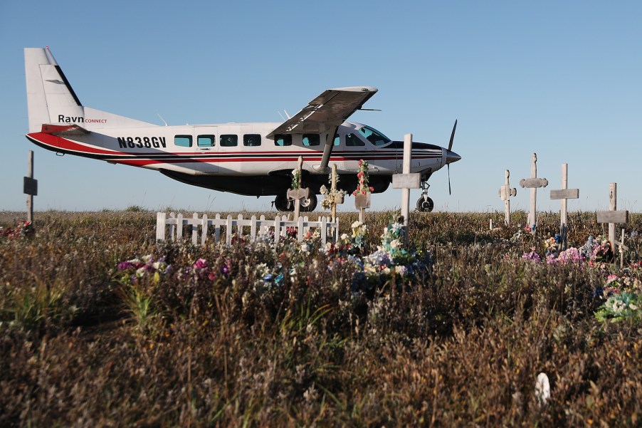 This is a commuter plane parked by a cemetery on a dirt runway in Alaska. Alaska has the highest rate of deadly plane crashes in the country.