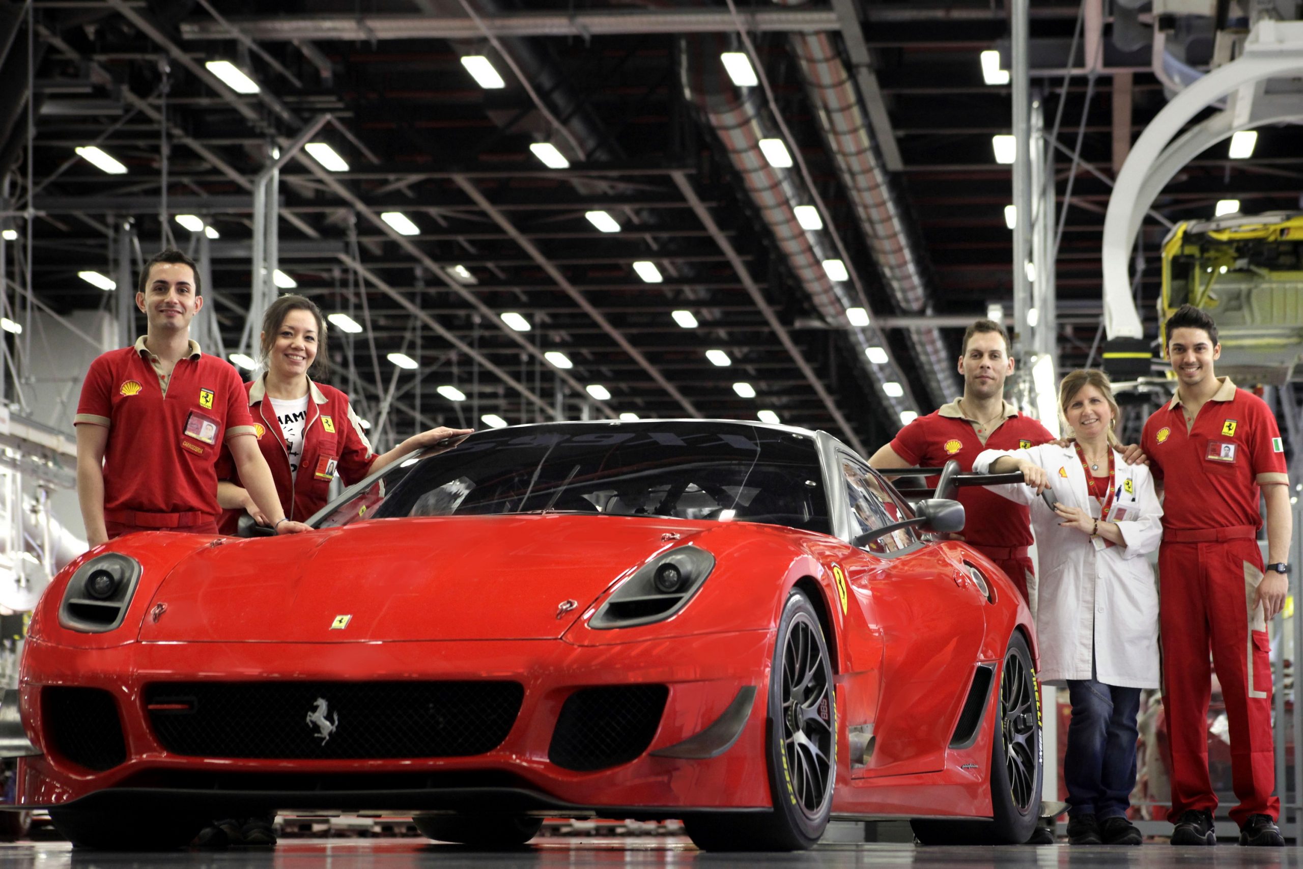 A handful of Ferrari factory workers, dressed in red, stand next to a complete Ferrari 599xx Evolution in Maranello