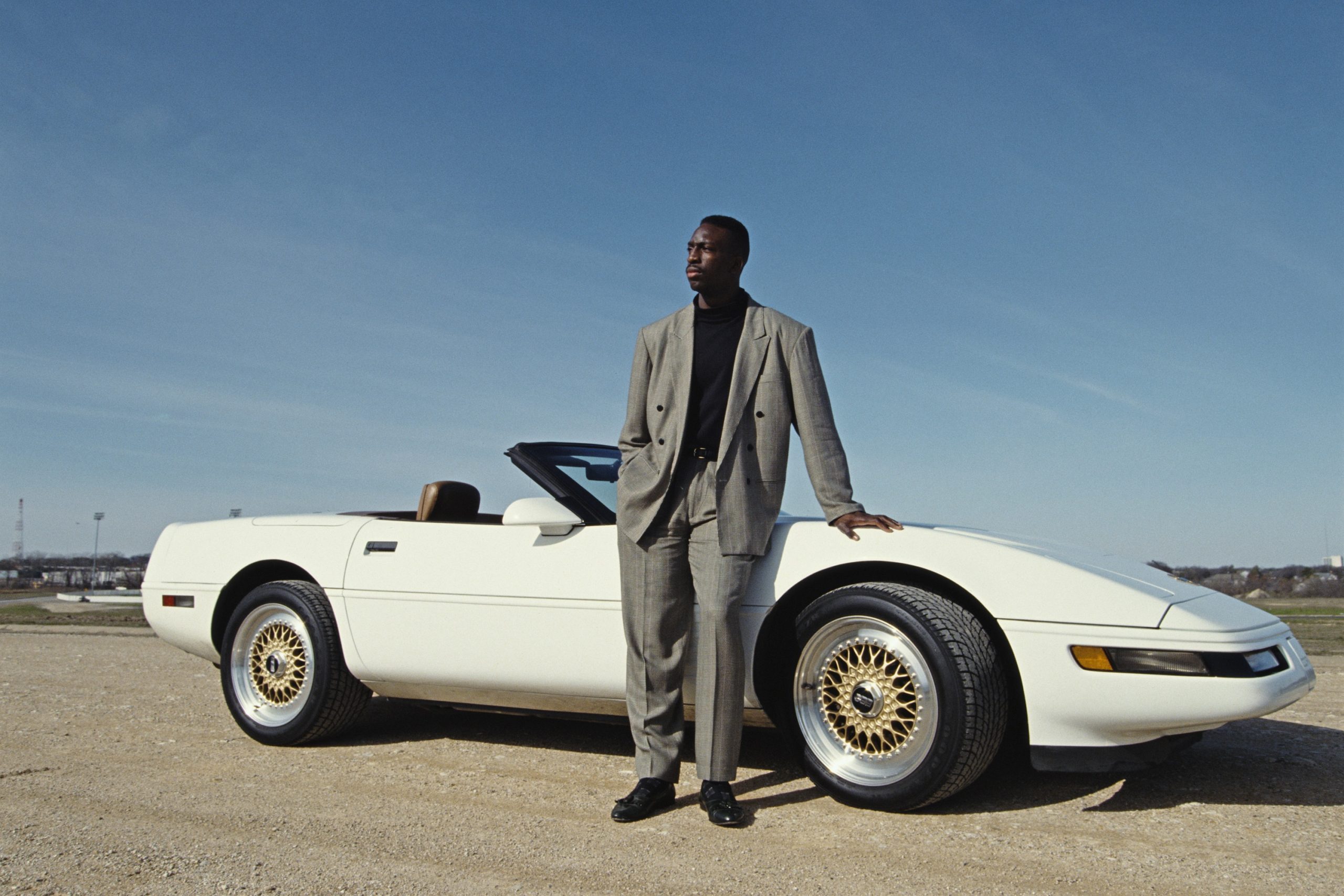 Olympic runner Michael Johnson stands in front of his white C4 convertible with BBS gold wheels