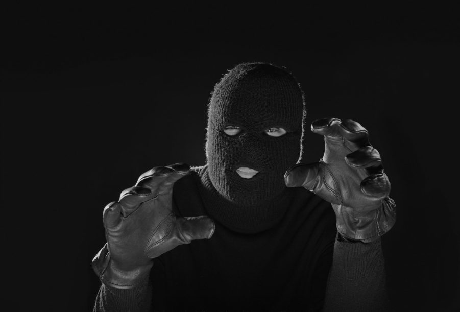 A man in a balaclava raises his gloved hands towards the camera