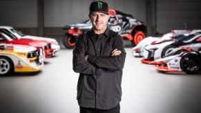 Rally racer Ken Block standing in a room with Audi rally cars and other race cars behind him