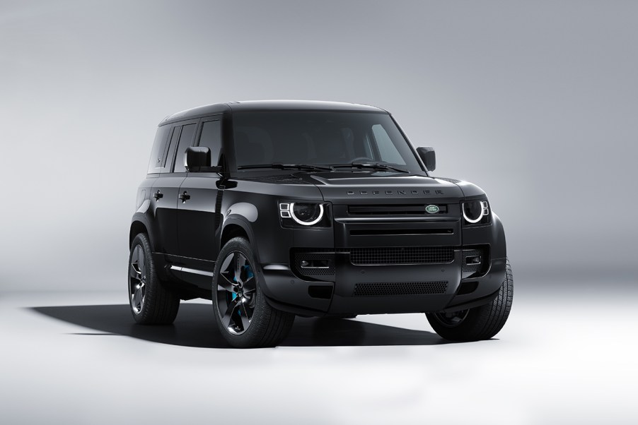 Land Rover Defender V8 Bond Edition in all black. Photo shot in a white studio. Vehicle is facing the camera with the front wheels slightly turned to the viewer's right, revealing a hint of the blue brake calipers.