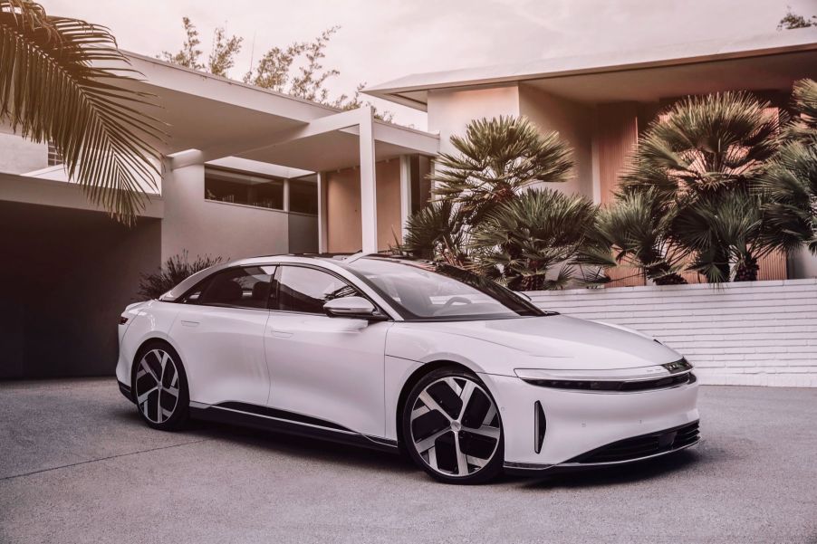 A white Lucid Air in front of a modern style home with palm trees.