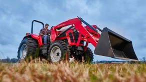 A farmer operates a red Mahindra 5100 Series utility tractor in a field