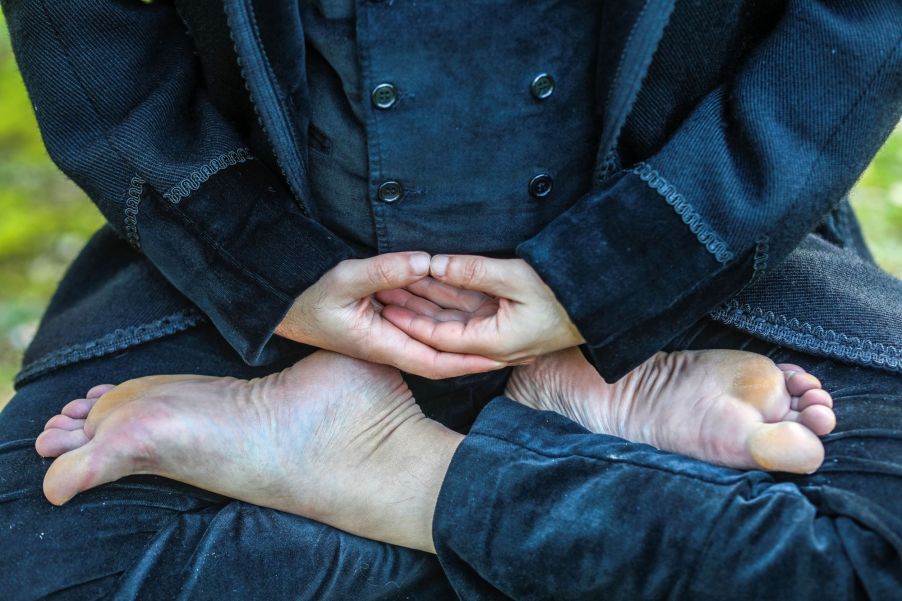 A man dressed in black in a meditation stance with feet crossed and hands in lap.