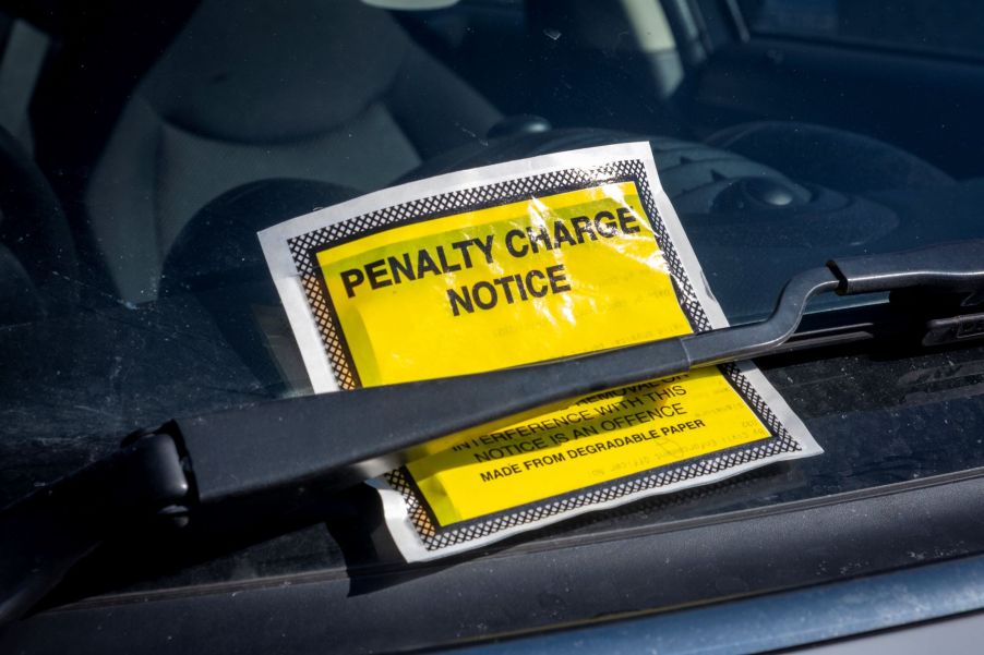 A bright yellow parking violation ticket on a vehicle under the windshield wiper.