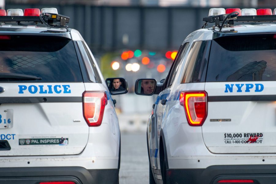 Two police cars, who could find a stolen car, parked beside each other with lights in the background.