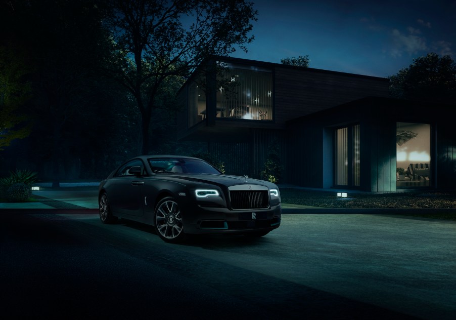 A dark-colored Rolls-Royce Wraith Kryptos parked in front of a modern house at night