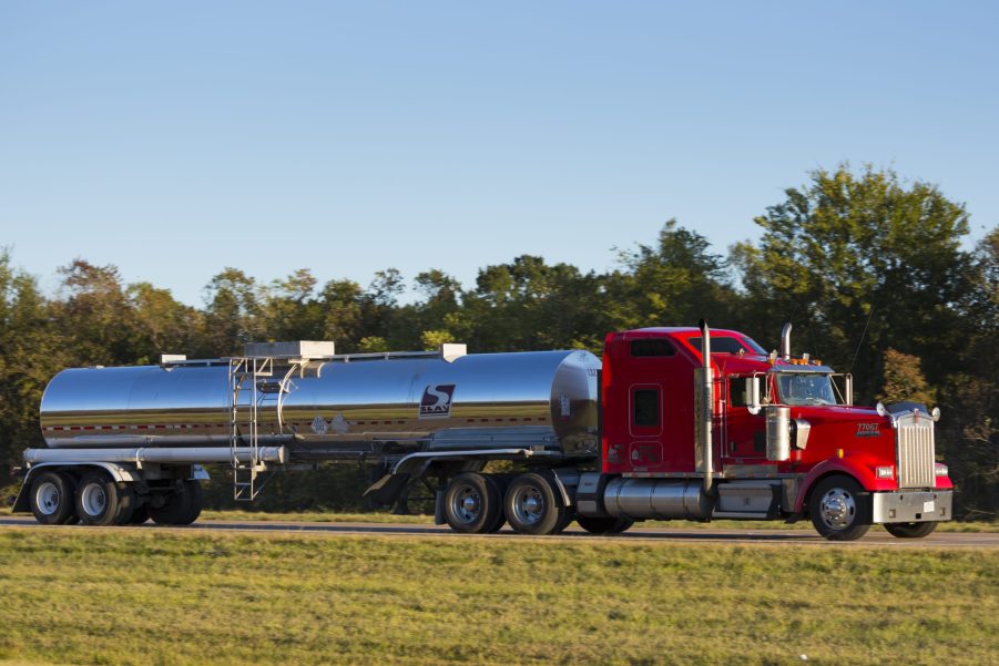 A red semi truck drives down the highway hauling an oil tanker