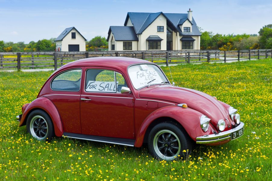 A red Volkswagen Beetle with a 'For Sale' sign for under $7,000 on its windshield parked in a field of flowers in Taghmon, Ireland