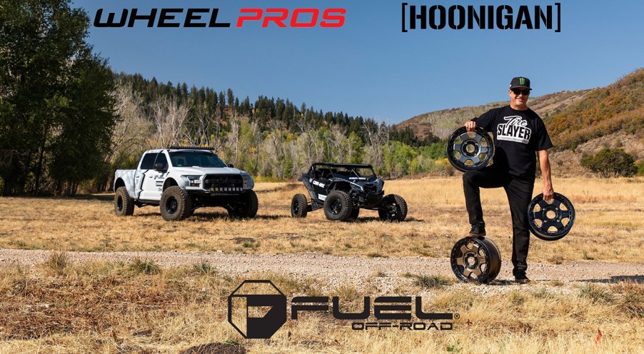 Ken Block's Hoonigan automotive lifestyle brand announces merger with Wheel Pros. Image of Ken Block holding off road wheels in each hand and another wheel under his left foot.