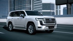 White 2022 Toyota Land Cruiser driving by tall buildings