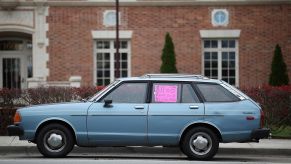 A used wagon parked on a street with a sale sign sitting in its window