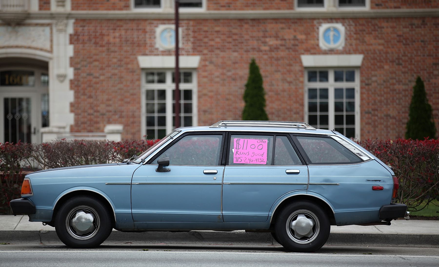 A used wagon parked on a street with a sale sign sitting in its window