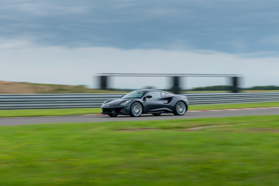 A black Lotus Emira on a racetrack, shot from afar in profile