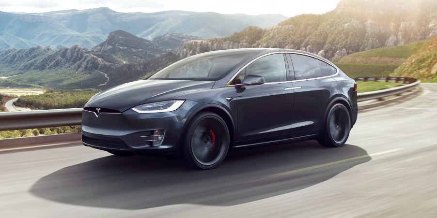 A dark gray Tesla Model X driving past mountains.