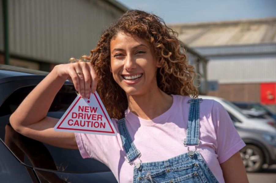 A new driver with their learner's permit holding up a car sticker