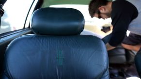 An old leather car seat in a Lincoln model as a man salvages upholstery in the background