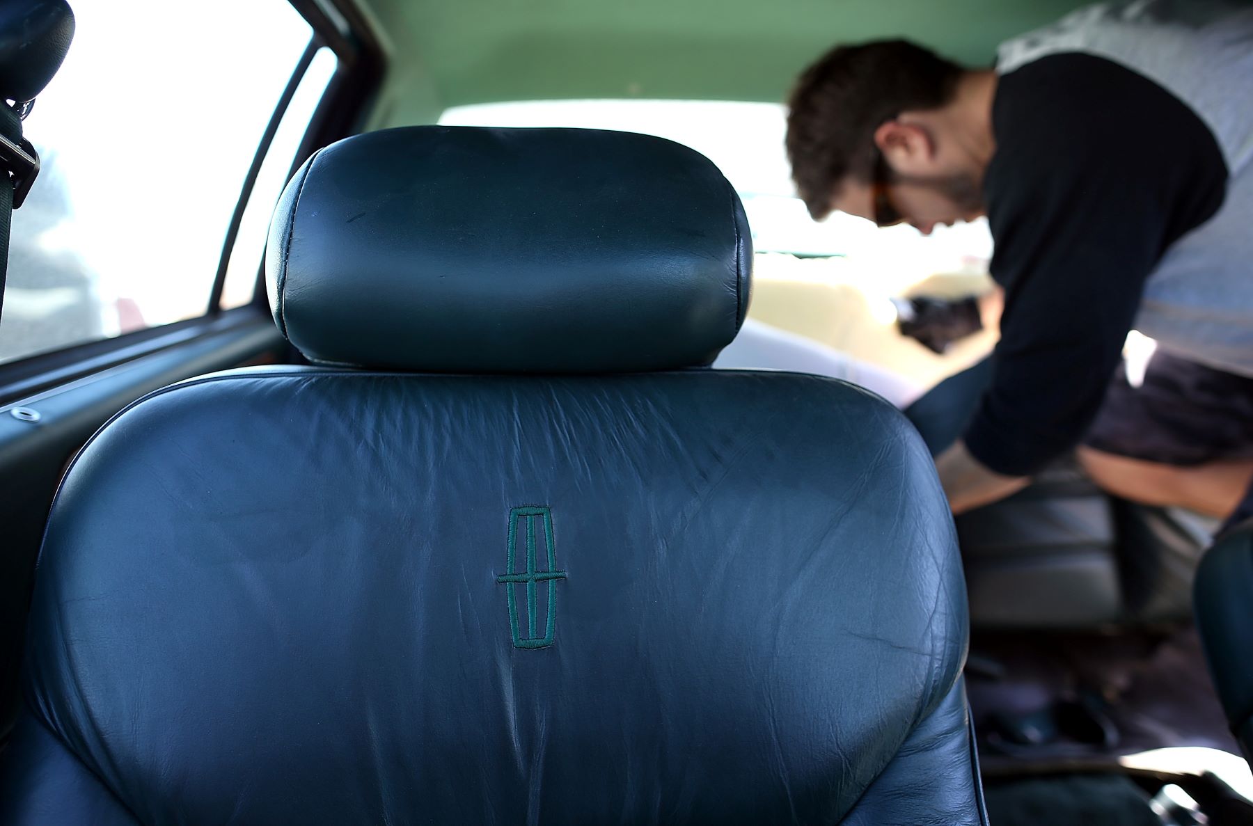 An old leather car seat in a Lincoln model as a man salvages upholstery in the background