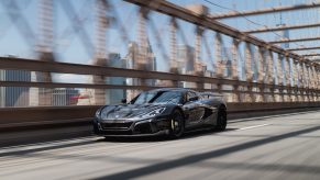 A grey Rimac Nevera, arguably the king of the electric supercars, drives down a bridge shot from the front 3/4.