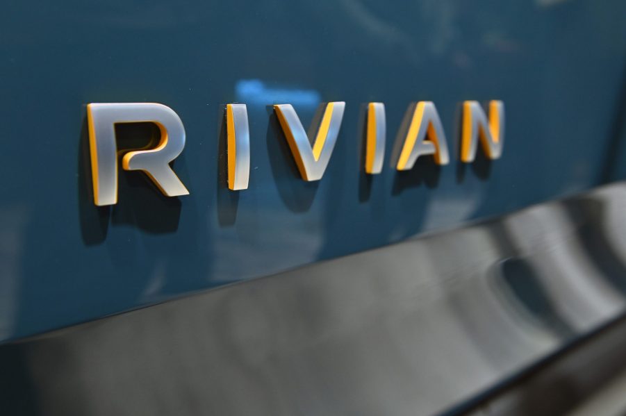 A grey Rivian logo on the back of a blue R1T truck at an auto show