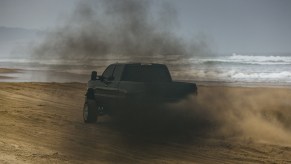 A black truck rolling coal on a beach.