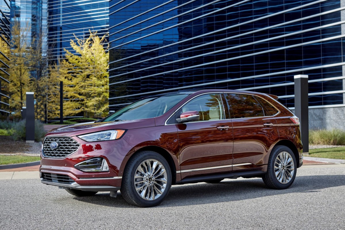 The 2021 Ford Edge Titanium Elite midsize SUV in dark red parked outside of a dark glass skyscraper