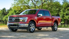 The 2021 Ford F-150 Lariat full-size pickup truck in red parked on a dirt country road near patches of forest