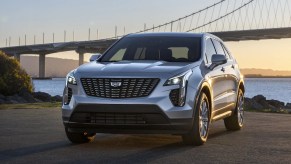 A silver Cadillac XT4 parked in front of a bridge at sunset.