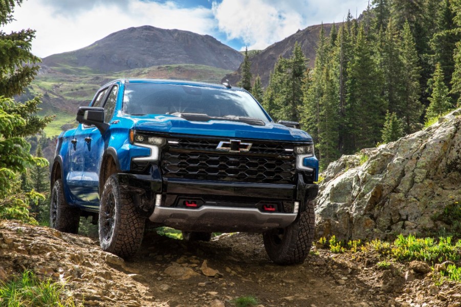 The 2022 Chevrolet Silverado ZR2 pick up truck painted in light blue driving towards the camera on a mountain path with lush green trees behind it. General Motors has just begun shipping out trucks again after production was paused due to the global semiconductor shortage