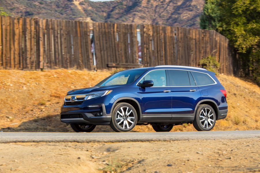 The 2022 Honda Pilot Elite SUV in blue parked in the desert near a wooden fence