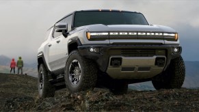 A white 2022 GMC Hummer parked on a mountain range with two people staring off into the sky in the background.