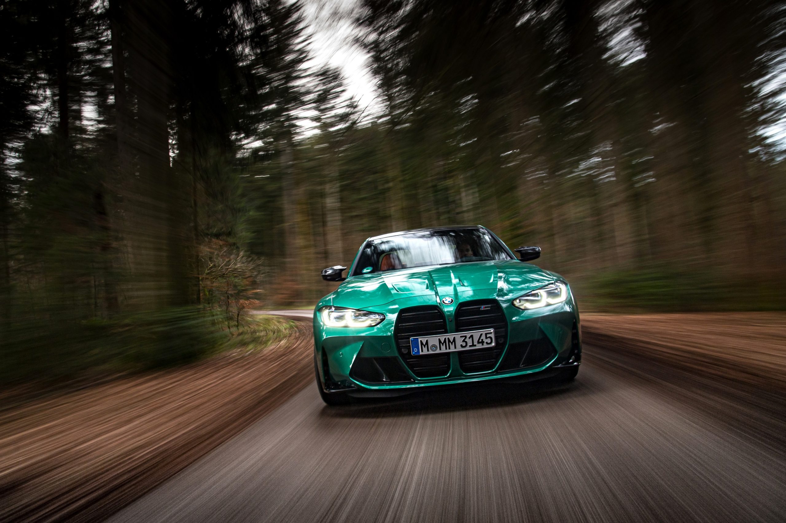 The 2022 BMW M3 Competition in Isle of Man Green shot from the front of a forested road