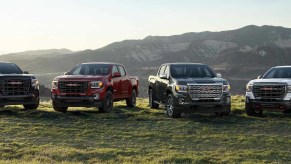 Four GMC pickup trucks parked in front of mountains.