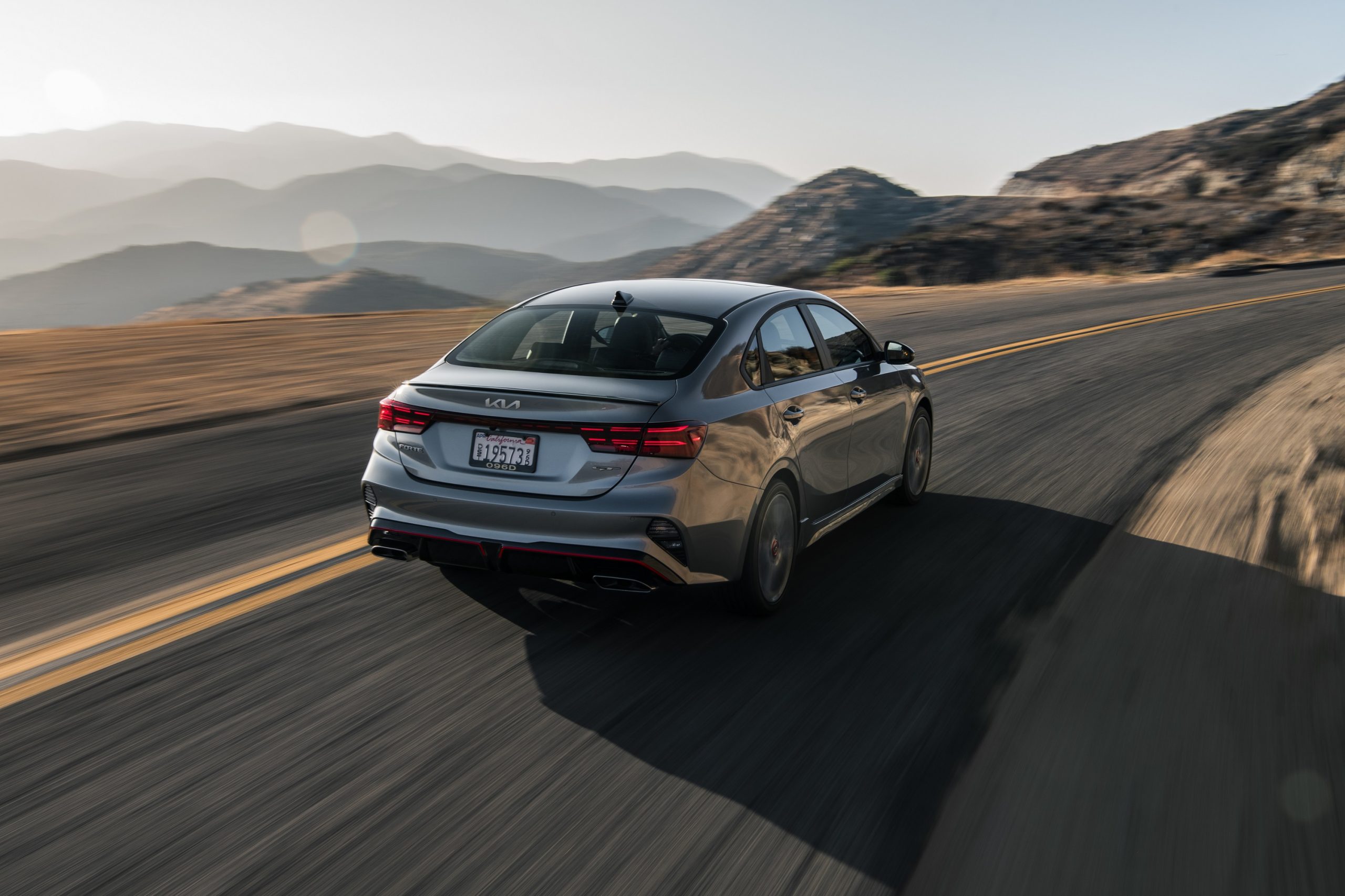 A silver Kia Forte GT shot from the rear on a canyon road