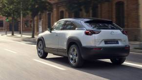 A white 2022 Mazda MX-30 driving down a city street.