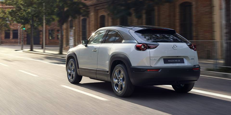 A white 2022 Mazda MX-30 driving down a city street. 