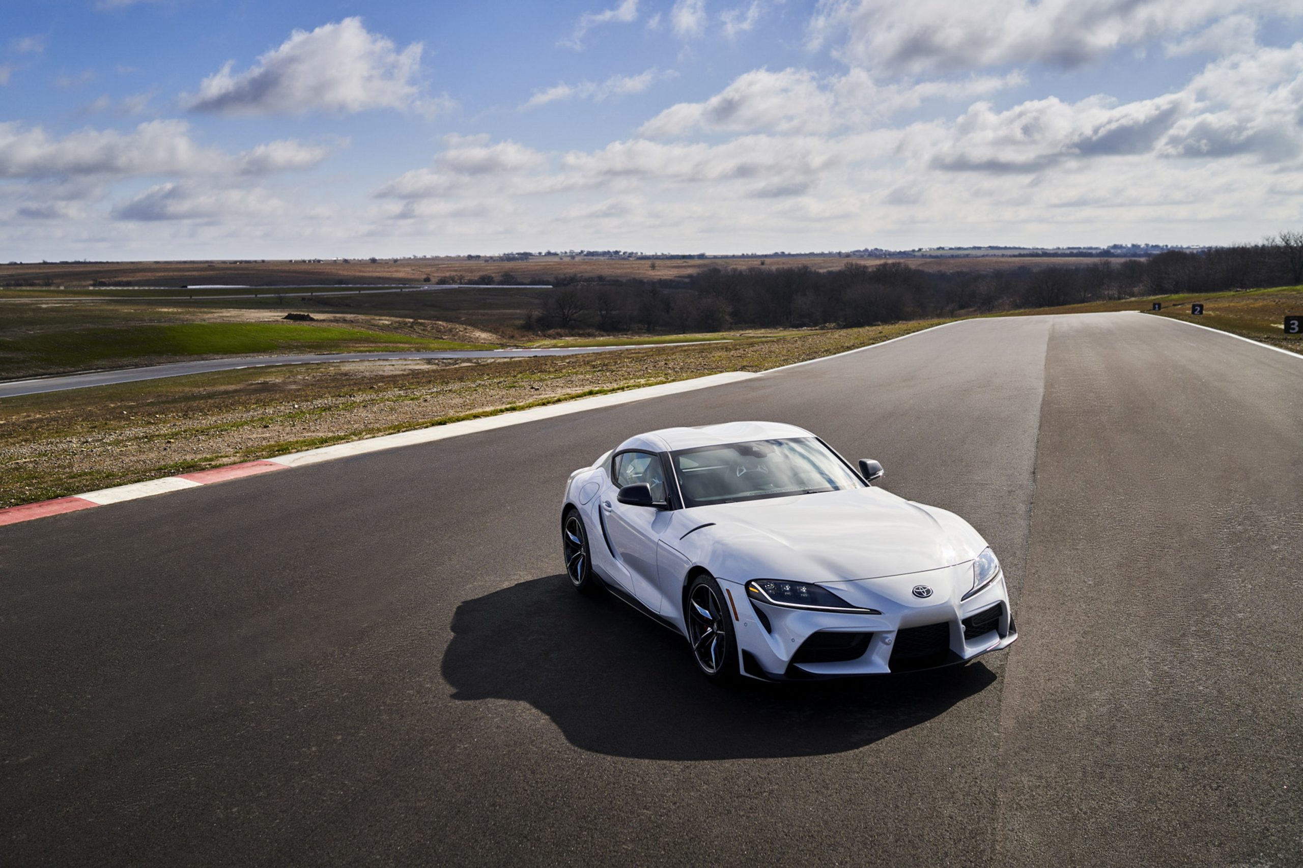 A white Toyota Supra 3.0 Premium shot on a racetrack from the high 3/4 angle