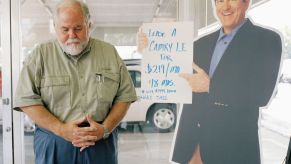 Car salesperson standing next to a cardboard cutout of another car salesperson