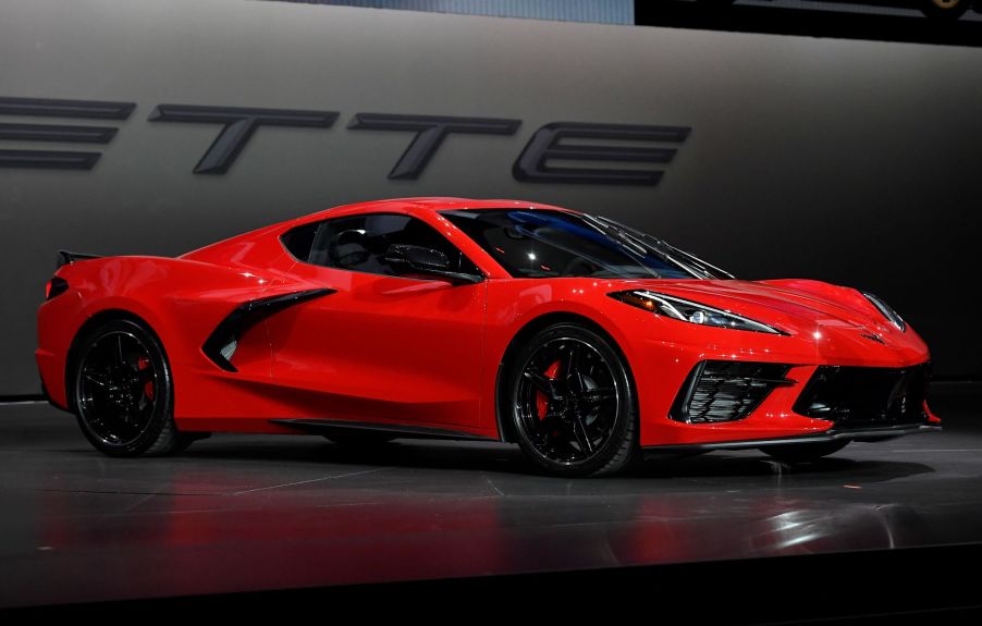 A red Corvette C8 in front of a black and grey background.