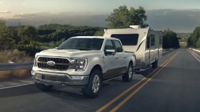 A white 2021 Ford F-150 pulling a trailer on the highway.