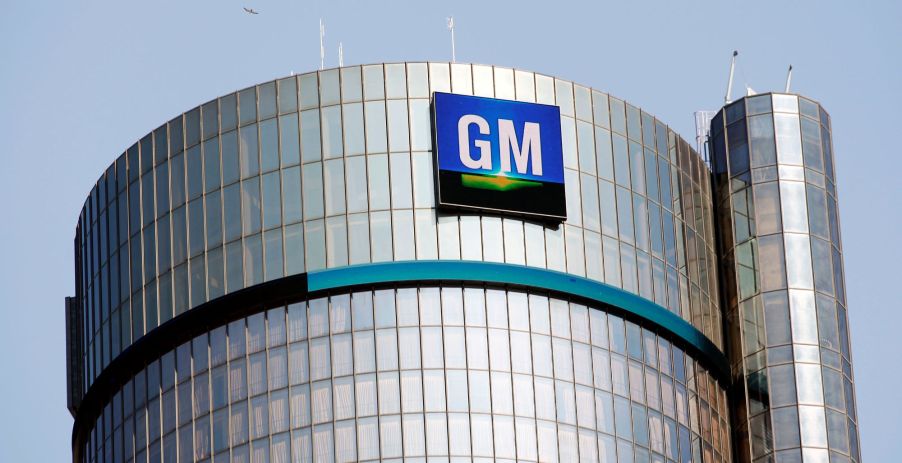 A silver building with a blue ring around the top in the shape of circle and the GM logo at the top. GM feels the microchip shortage.