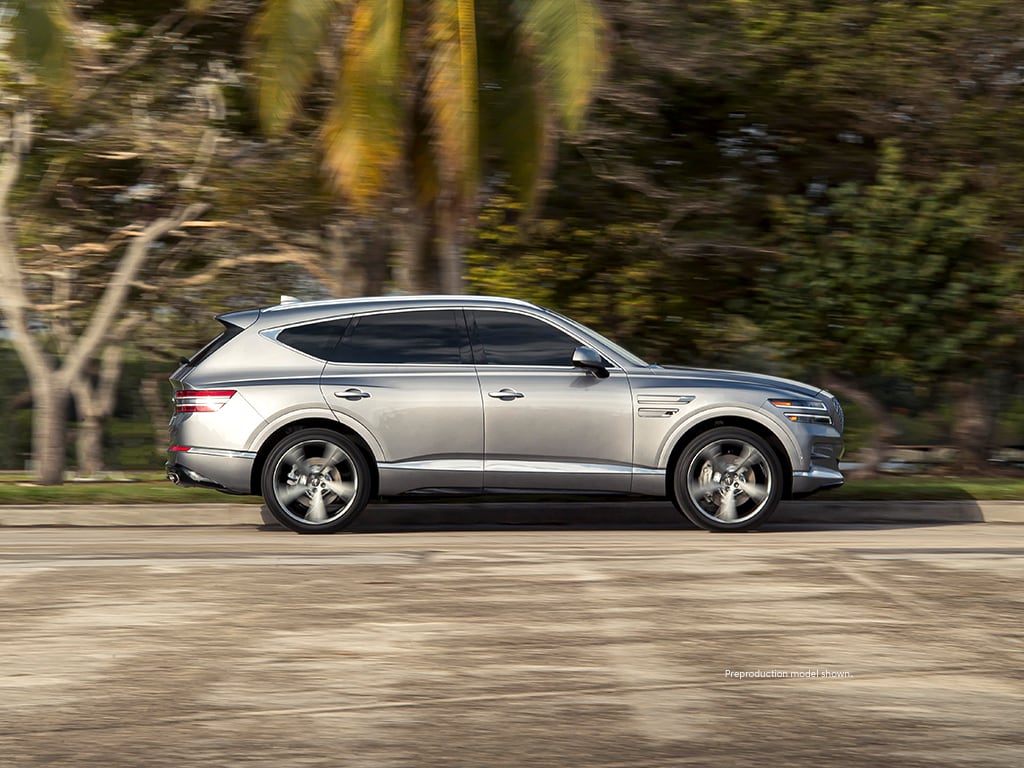 A silver Genesis GV80 parked by a bunch of trees