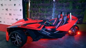 A red Polaris Slingshot sitting in front of a black and white background.